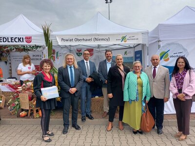 Acht Personen stehen vor einem Messestand vom Landkreis Oberhavel und l&auml;cheln in die Kamera.