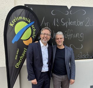 Zwei M&auml;nnermittleren Alters stehen neben einem Banner mit der Aufschrift Kreismusikschule Oberhavel.