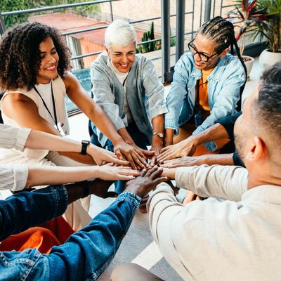 Diverse group of individuals join hands in a circle, symbolizing teamwork and unity during a collaborative meeting in a bright, modern office space.